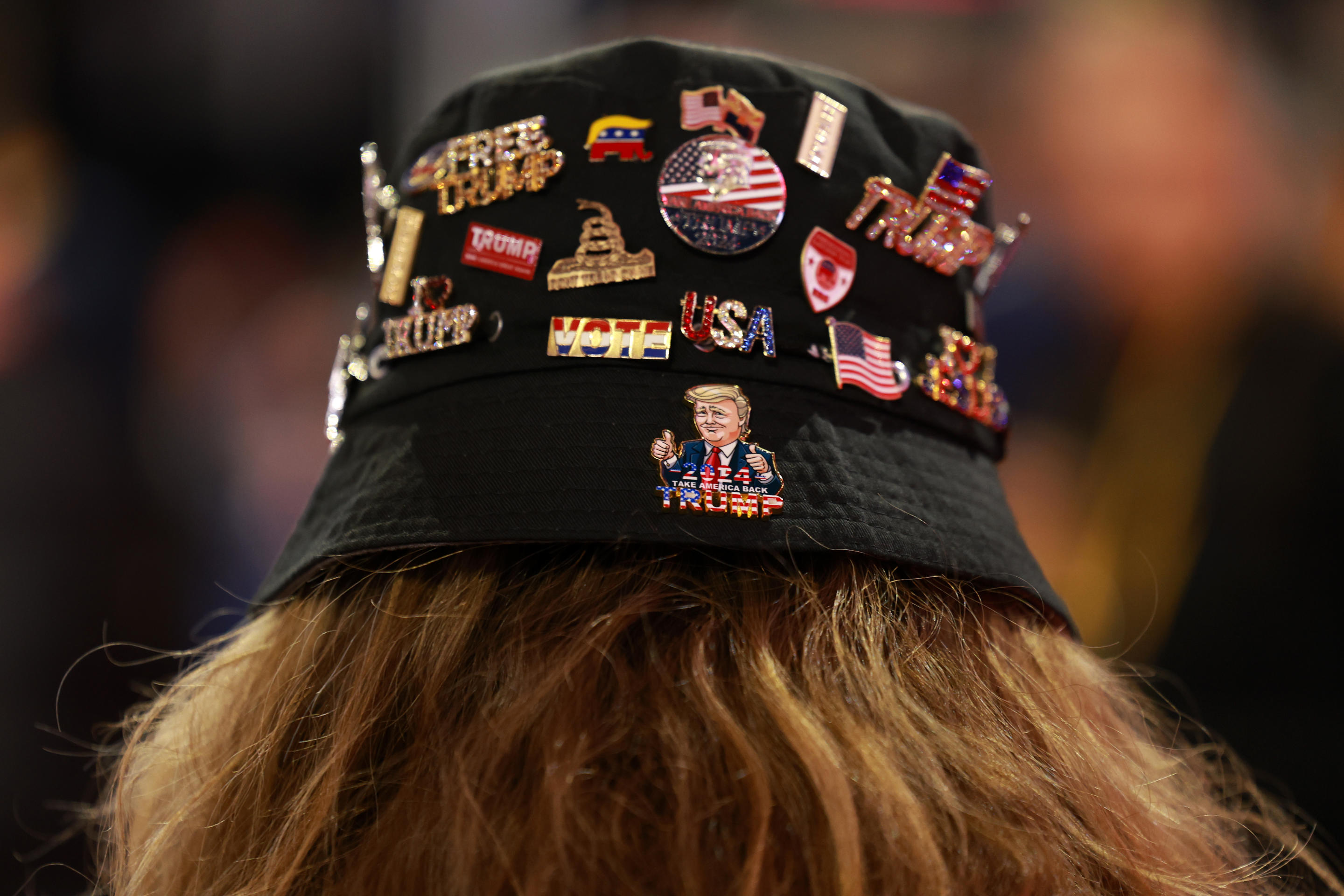 An attendee wears a hat covered in pins.  