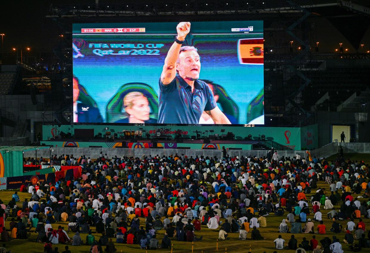 Qatar's migrant workers watch the Qatar 2022 World Cup round of 16 football match between Morocco and Spain with Spains head coach Luis Enrique on the video screen on December 6, 2022, at the Asian Town cricket stadium, on the outskirts of Doha. - The stadium has become a daily draw for thousands of the poorest workers who live in nearby dormitories away from Doha's glitzy shopping malls and restaurants. (Photo by INA FASSBENDER / AFP) (Photo by INA FASSBENDER/AFP via Getty Images)