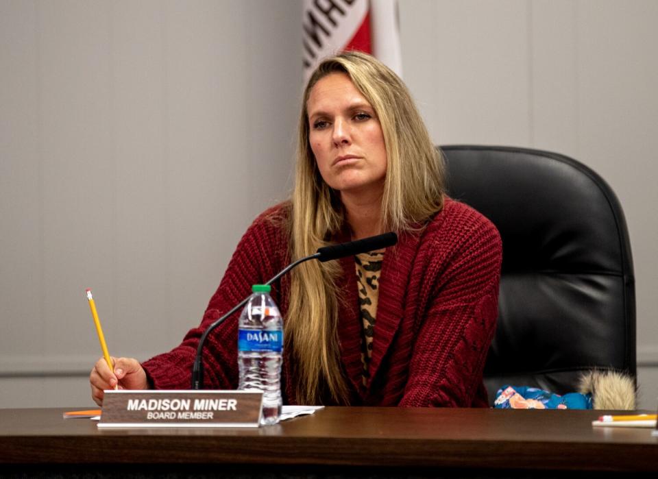 A woman sits behind a desk holding a pencil, looking past the camera on right.