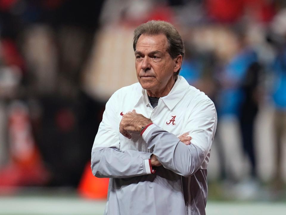 Nick Saban stands with his arms folded while on the field in 2021.