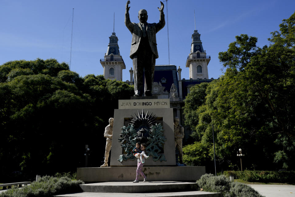 Aksinia Domini, 6, carries her 3-year-old sister Agata, in front of a monument honoring former Argentine President Juan Domingo Peron, at a park in Buenos Aires, Argentina, Saturday, April 22, 2023. The girls' parents are part of an increasing number of Russians from the LGBTQ+ community who left their homeland to escape both discrimination and the war with Ukraine and settled in Argentina. (AP Photo/Natacha Pisarenko)