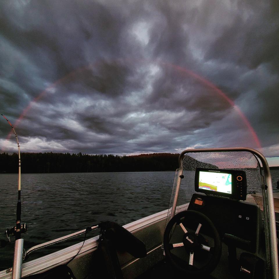a boat out on a lake, a cloudy night, and a full arc rainbow that's only red