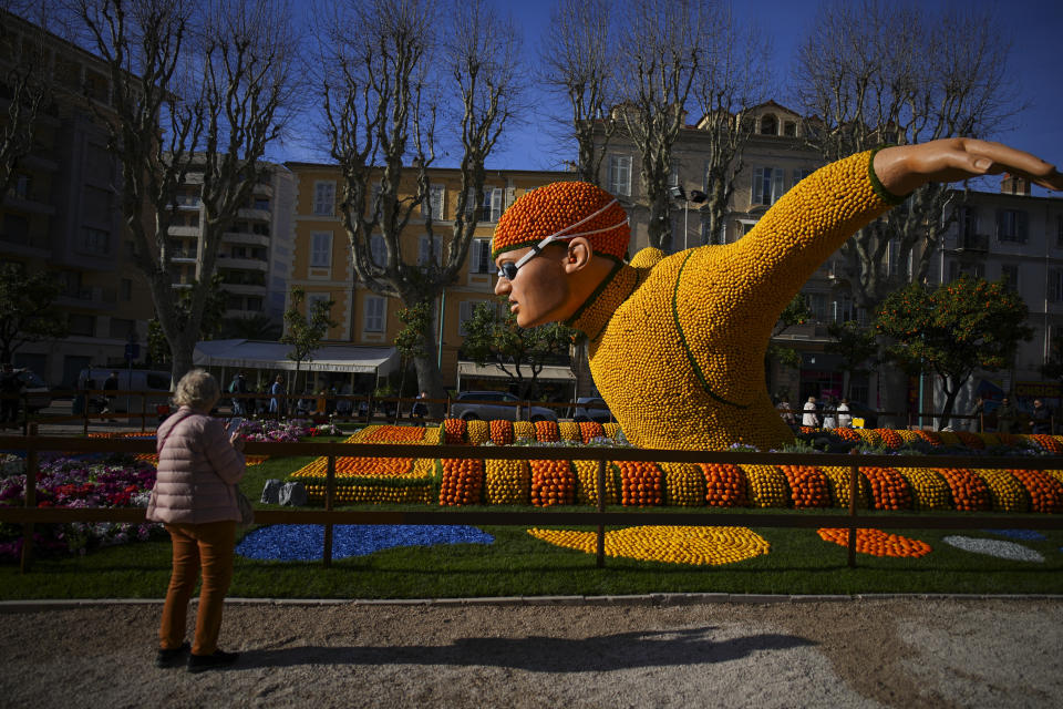 A woman stands next to an olympic swimmer sculpture made with lemons during the 90th Olympia in Menton edition of the Lemon Festival in Menton, southern France, Saturday, Feb. 17, 2024. (AP Photo/Daniel Cole)