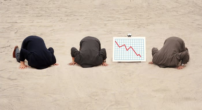 Three businessmen sticking their heads in the sand as a chart next to  them shows a red down arrow.