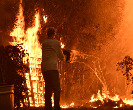 A resident pours a bucket of water to put out flames caused by the Woosley Fire in Malibu, California, U.S. November 9, 2018. REUTERS/Gene Blevins