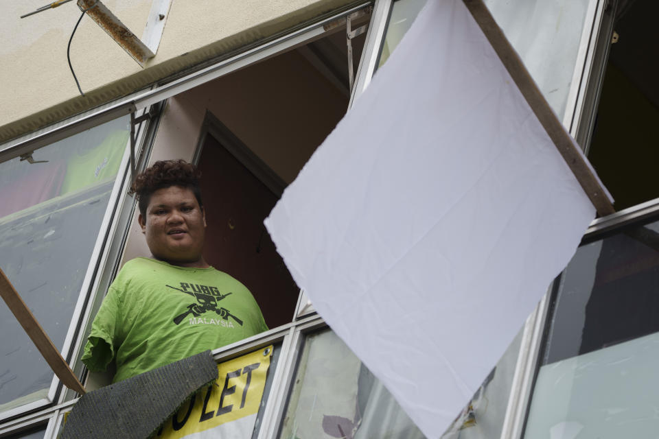 Mohamad Nor Abdullah, born without arms, looks out from a window near a white flag outside the window of his rented room in Kuala Lumpur, Malaysia on July 3, 2021. When Mohamad Nor put a white flag outside his window late at night, he didn’t expect the swift outpouring of support. By morning, dozens of strangers knocked on his door, offering food, cash and encouragement. (AP Photo/Vincent Thian)