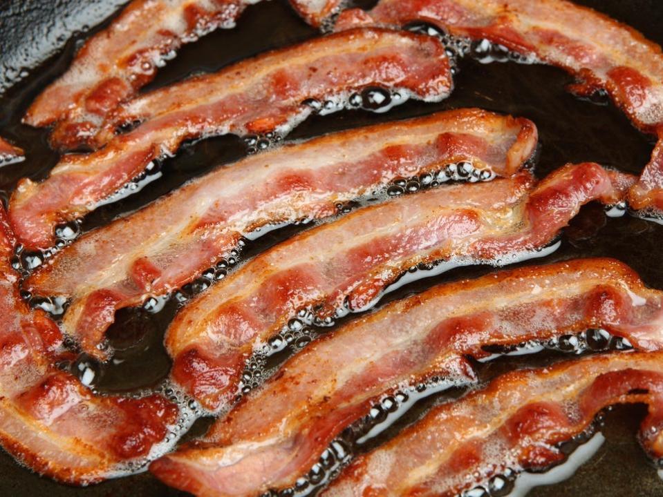 Bacon slices frying in grease in pan