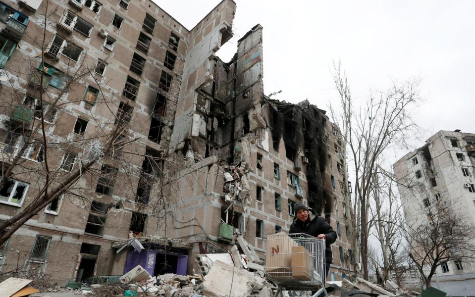 A local resident pushes a cart with humanitarian aid past an apartment building damaged during the war in the southern port city of Mariupol, Ukraine on April 4, 2022. - Alexander Ermochenko/Reuters