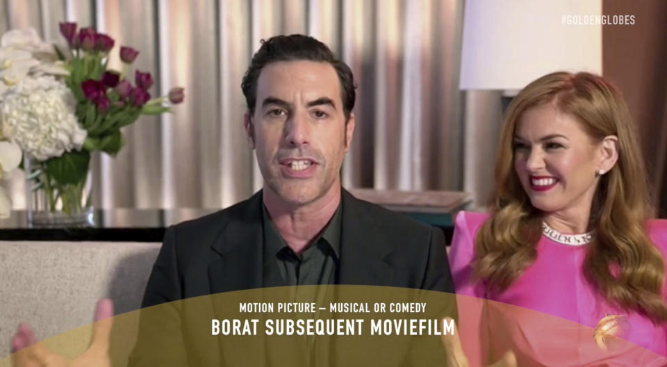 En esta imagen difundida por NBC el domingo 28 de febrero de 2021, Sacha Baron Cohen, a la izquierda, acepta el Globo de Oro a la mejor película musical o de comedia, por "Borat Subsequent Moviefilm", junto a su esposa, la actriz Isla Fisher. (NBC via AP)