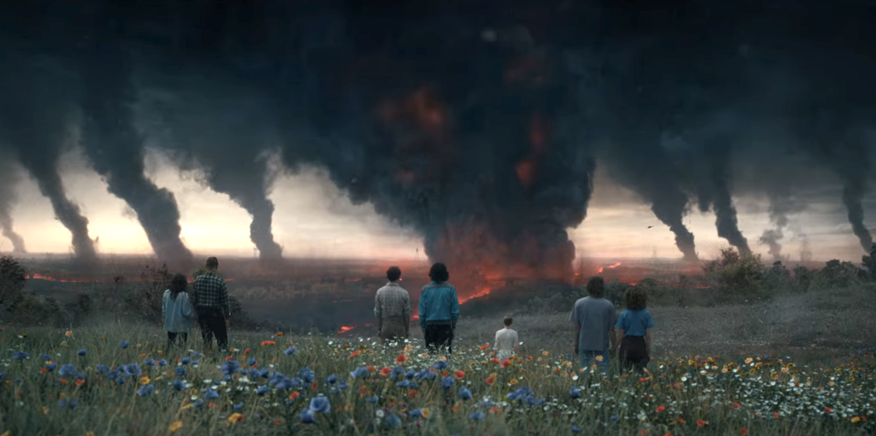 People in a field with flowers and looking at fire and smoke