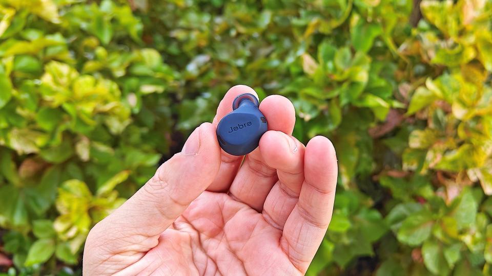 Jabra Elite 8 Active earbuds held in hand with a green hedge in the background