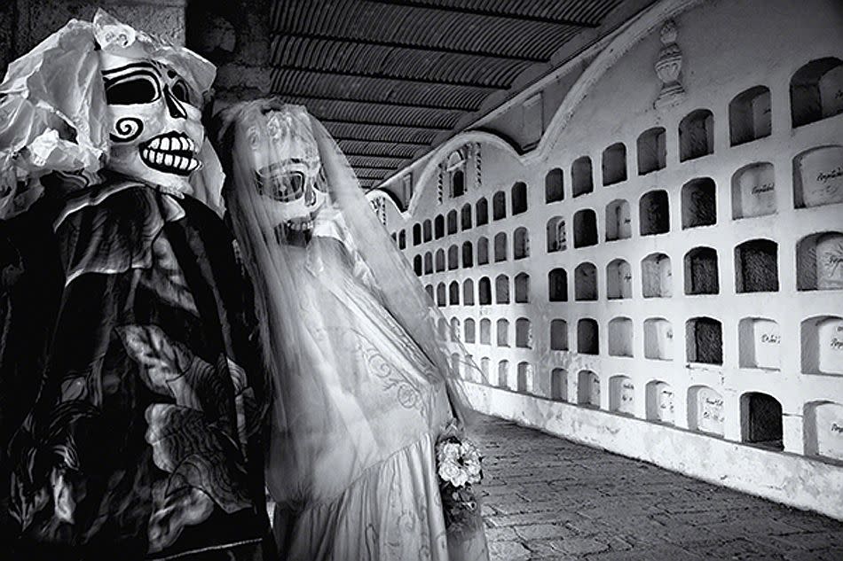 Oaxaca, Mexico. Dia de los Muertos (Day of the Dead). <br><br>La Calavera Catrina (The Elegant Skull) is a popular icon of the festival and here two large Catrinas set up in the cemetery seem to smile on the tombs lining the wall. <br><br>Camera: Canon EOS 5D MkII Louis Montrose, USA <br><br>Overall winner – Travel Photographer of the Year 2011