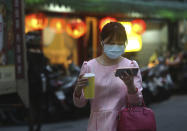 A woman her protective face mask balances her large-sized cup while watching her smart phone in Taipei, Taiwan, Tuesday, March 31, 2020. The new coronavirus causes mild or moderate symptoms for most people, but for some, especially older adults and people with existing health problems, it can cause more severe illness or death. (AP Photo/Chiang Ying-ying)