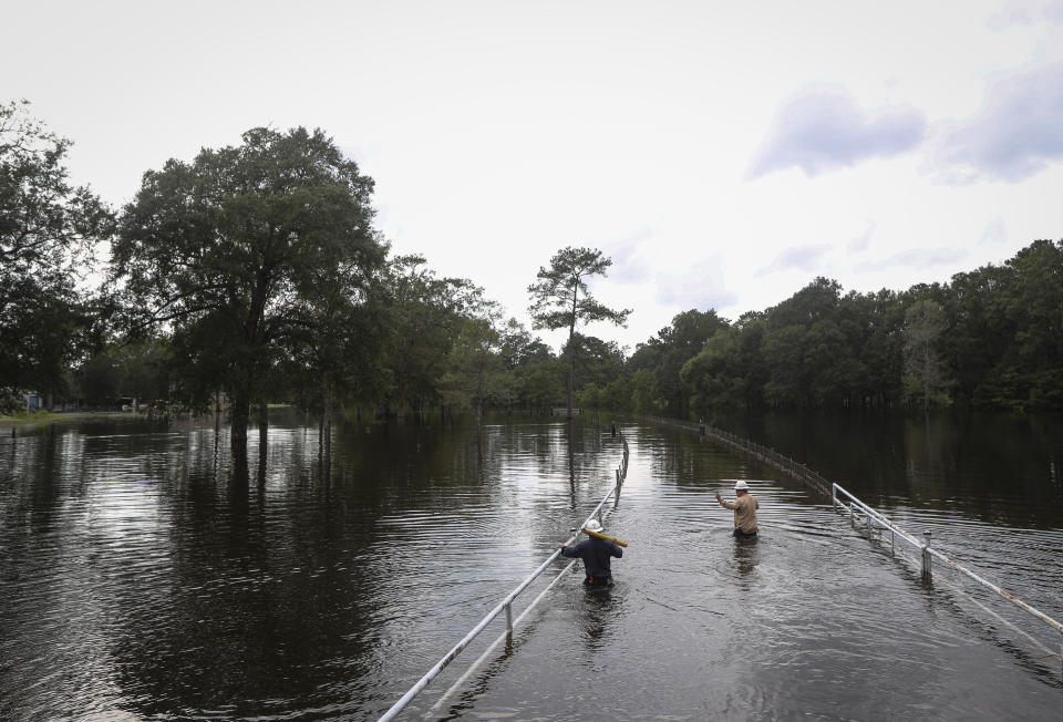 Mike Davis, left, and Trent Tipton, both line workers from Woodville, Texas, walk through floodwater to try to restore power for a customer on Friday, Sept. 20, 2019, in the Mauriceville, Texas, area. Floodwaters are starting to recede in most of the Houston area after the remnants of Tropical Storm Imelda flooded parts of Texas. ( Jon Shapley/Houston Chronicle via AP)