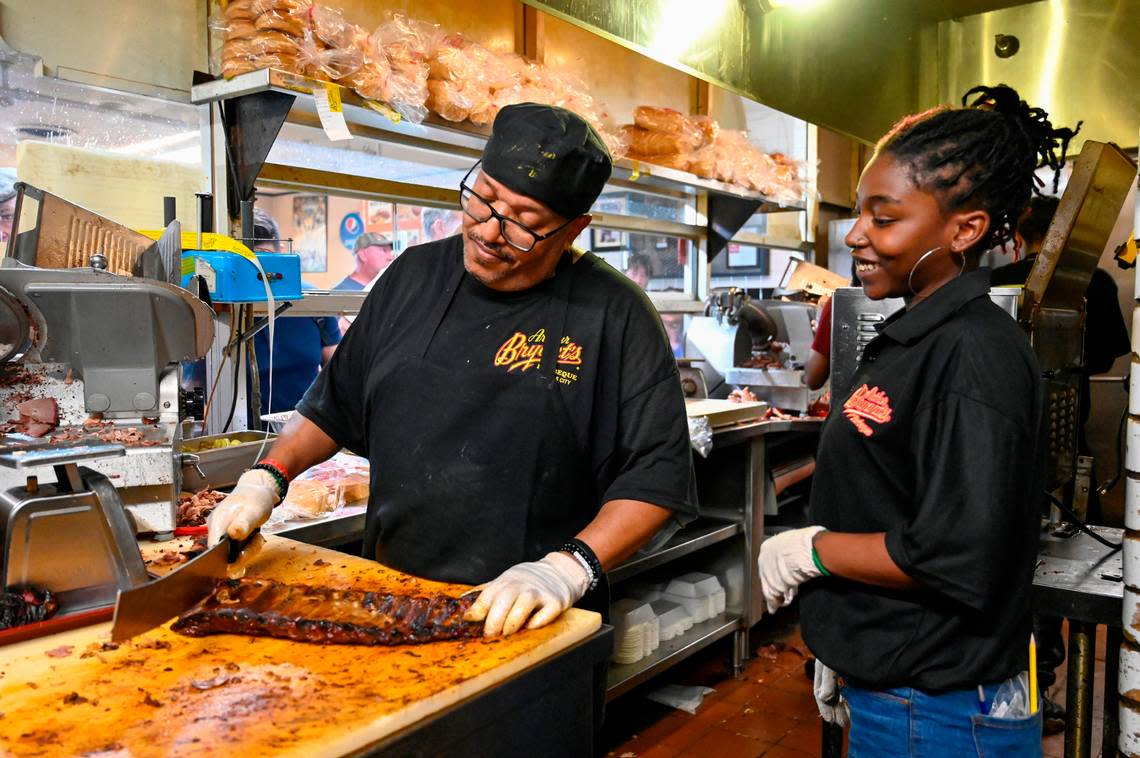 Larry Ashley wields a large knife as he slices a slab of ribs while manager Raven Watts looks on in the kitchen at Arthur Bryant’s Barbeque.