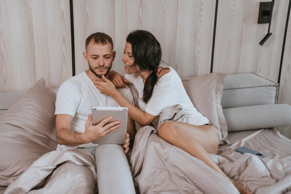 a woman trying to get her husband's attention in bed while he stares at a tablet