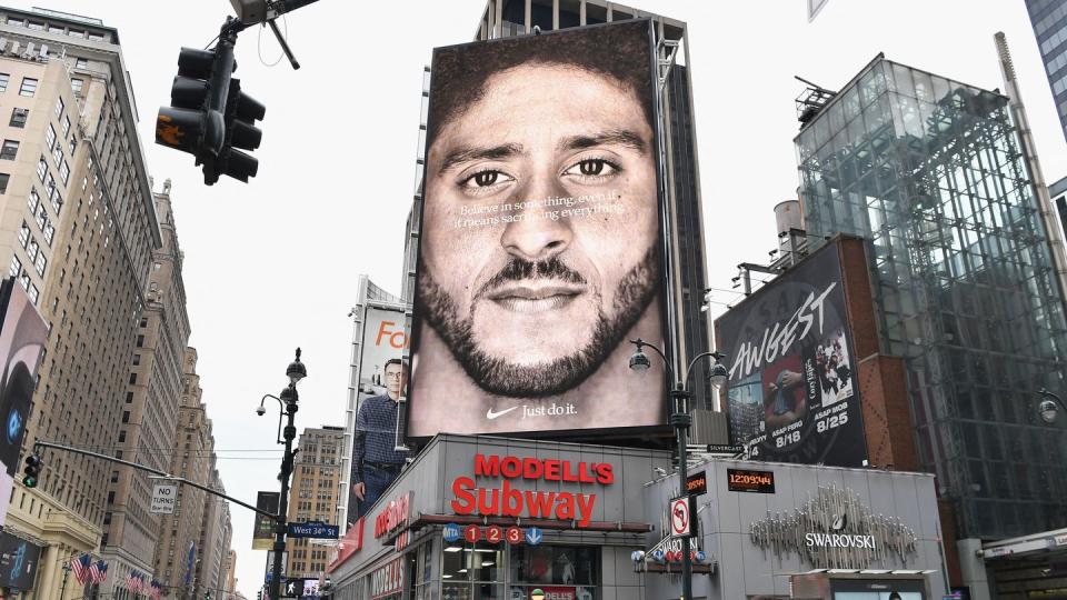 a city corner in new york city featuring a large nike ad with colin kaepernick, above a subway entrance