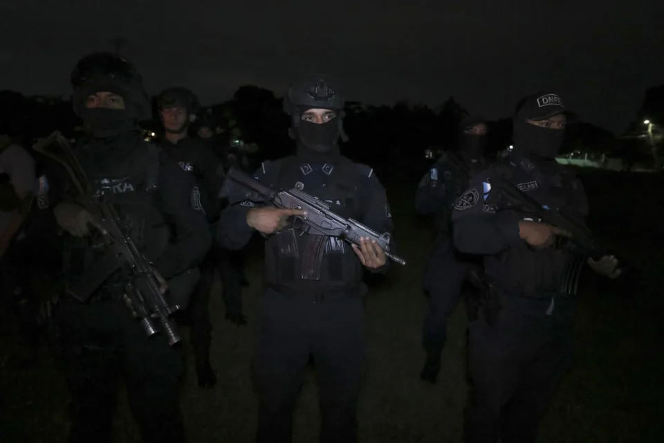 A group of officers in dark uniforms wielding assault weapons