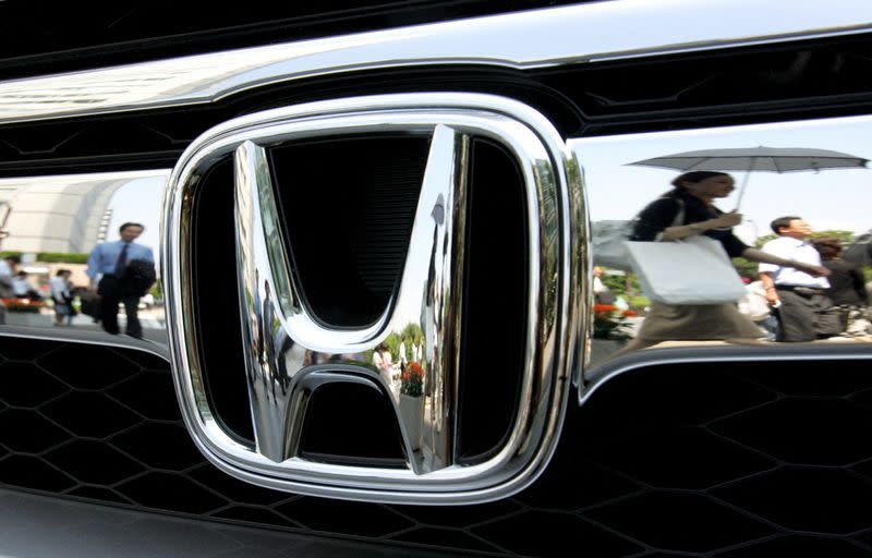 FILE PHOTO: Pedestrians are reflected on Honda Motor Co. badge outside company headquarters in Tokyo