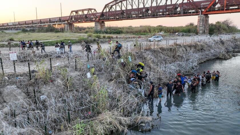 Eagle Pass, Texas, Saturday, September 23, 2023 - People who crossed the U.S./Mexico border look for a passage way through razor wire on the Texas side of the Rio Grande. (Robert Gauthier/Los Angeles Times)