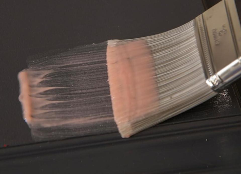 A paint brush brushes citrus paint remover onto wood that's painted brown.
