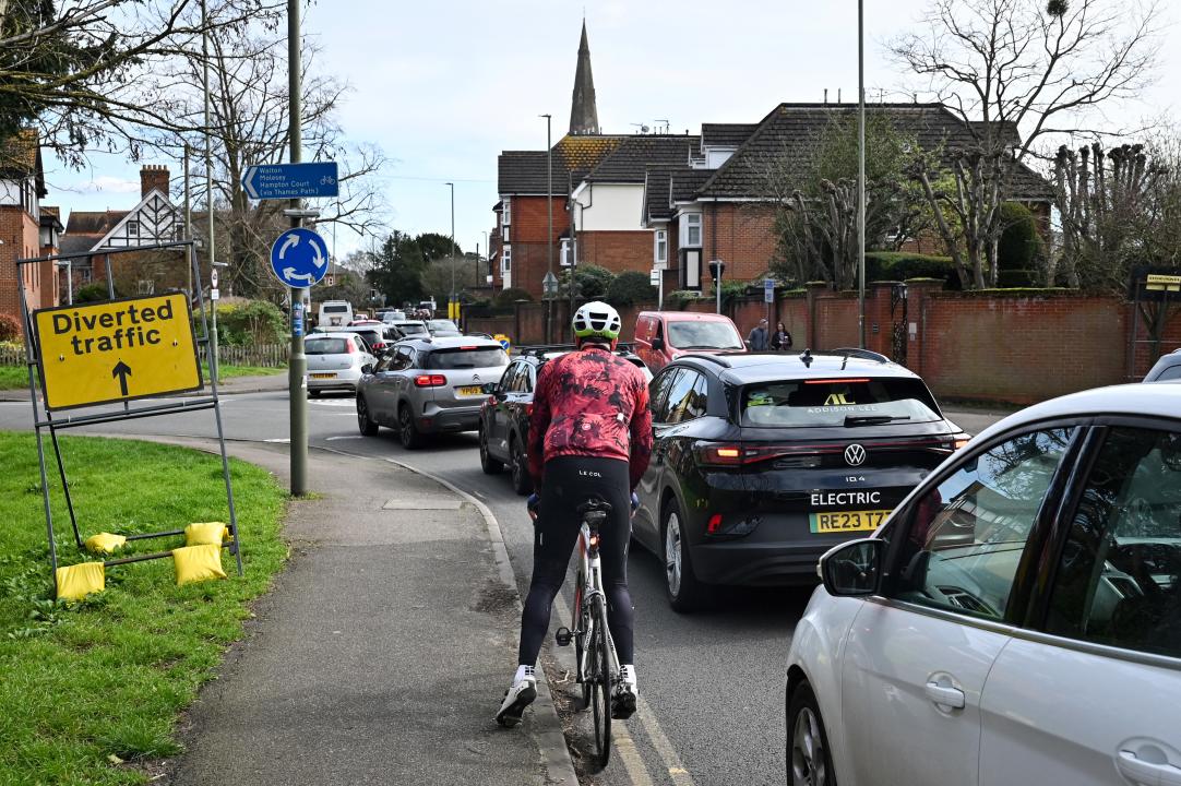 A cyclist makes his way through vehicles queueing along the street going into Weybridge south-west of London on March 16, 2024, as the London orbital motorway M25 sees it's first total closure over a weekend since it's opening in 1986. The M25 will be closed between junctions 10 and 11 from Friday 15 March 2024 evening until Monday 18 March 2024 morning to demolish the Clearmount bridleway bridge and install a very large gantry. (Photo by JUSTIN TALLIS / AFP) (Photo by JUSTIN TALLIS/AFP via Getty Images)
