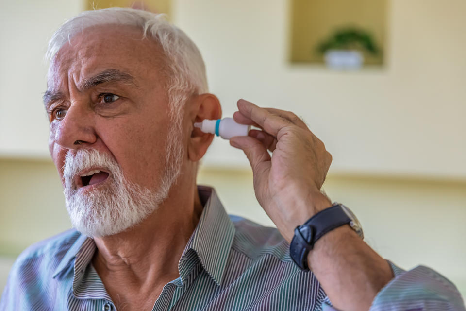 A Senior Bearded Man is Dropping Liquid in his Ear with Pipette. Medicine Health Concept.