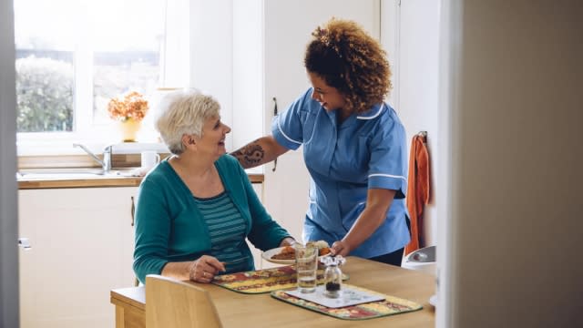 Care worker giving older lady her dinner in her home.