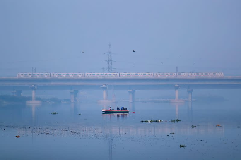 People ride a boat across Yamuna river as a metro train is seen in the background in New Delhi, India