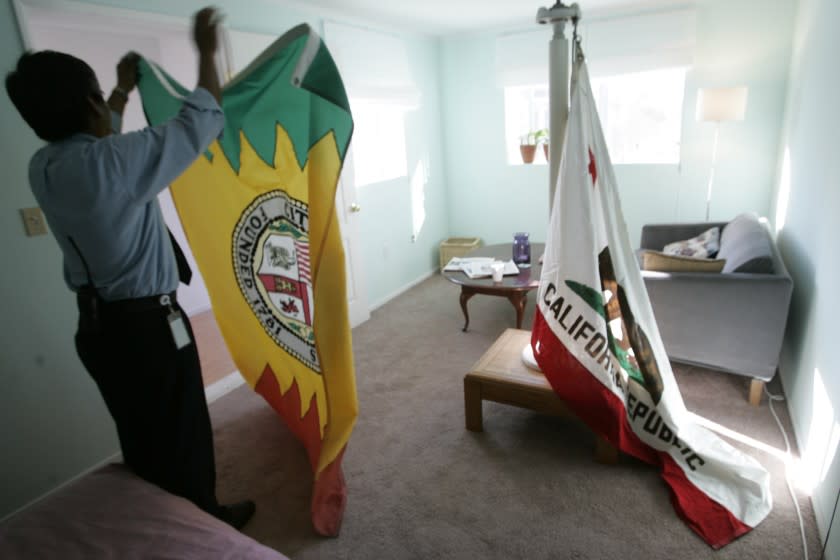 Security guard Medardo Villahermosa, folds up the city flag of Los Angeles, after replacing it with the California State flag, right, inside the Kariforunia art tower exhibit located inside a room built above scaffolding on 1st St. in Downtown L.A. The city flag for Los Angeles was mistakenly put on display inside exhibit instead of the state flag.