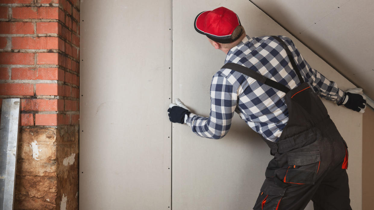 Man installing plasterboard sheet to wall for attic room construction.