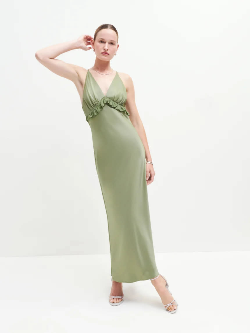 a model wears a sage green satin dress in front of a plain backdrop