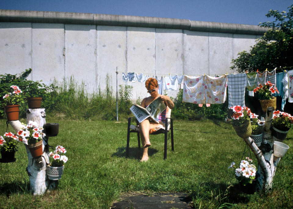 <p>Una mujer lee el periódico en su jardín, que está pegado al muro. (Photo by Thierlein/ullstein bild via Getty Images)</p> 