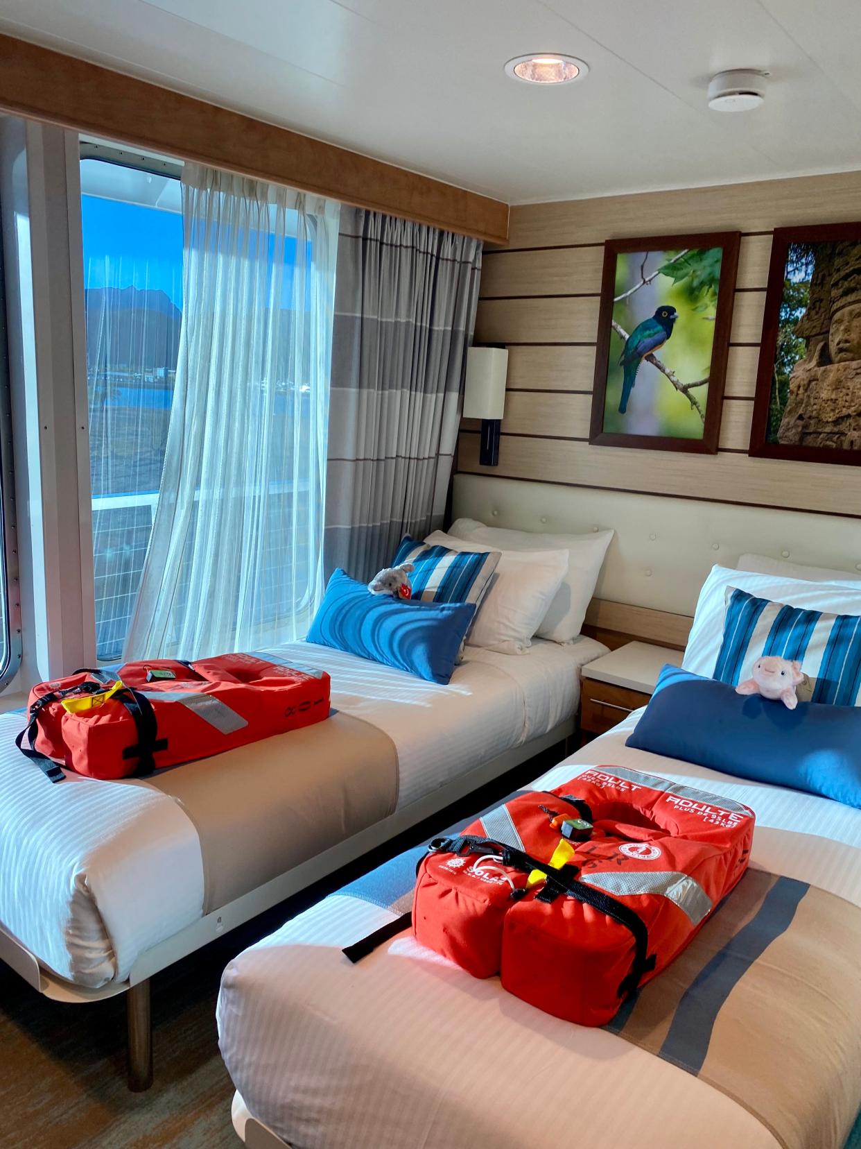 Lindblad Expedition- National Geographic cruise stateroom. Showing two twin beds with white linens, blue pillows, and orange life vests.