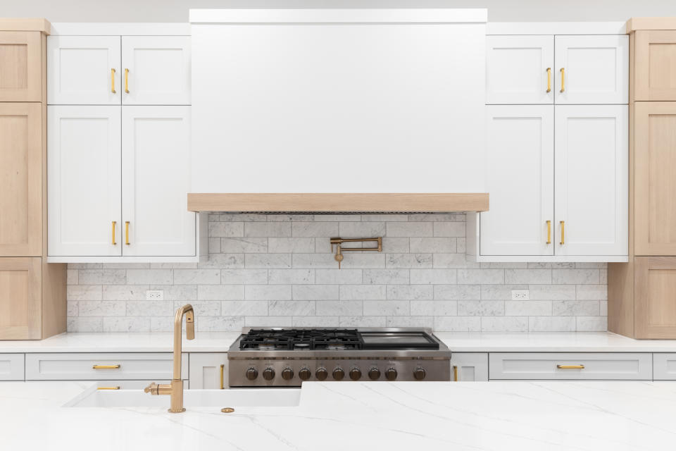 Modern kitchen with wooden cabinets, a marble countertop, and stovetop pot filler