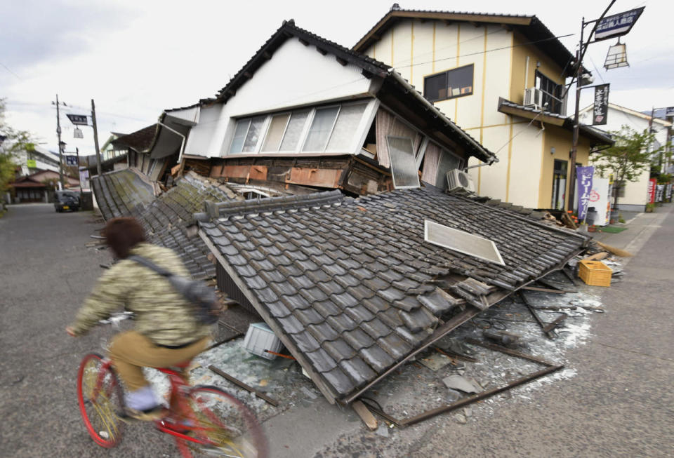 A cyclist passes collapsed houses