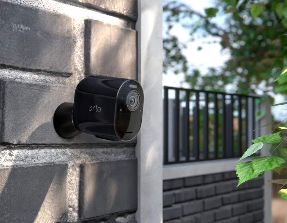 A close up of an Arlo security camera mounted on a brick wall.