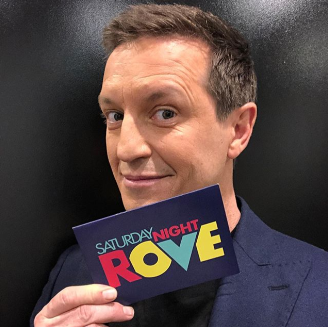 Rove McManus holding a cue card backstage on the TV set for Saturday Night Rove