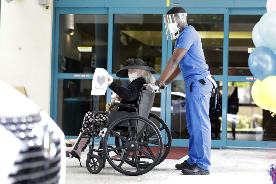 Margaret Choinacki, center, 87, who has no other family members left because her husband and daughter have died, waves goodbye after a drive-by visit by her friend Frances Reaves, as resident care coordinator Anggy Volmar, right, wheels her back inside, Friday, July 17, 2020, at Miami Jewish Health in Miami. Miami Jewish Health has connected more than 5,000 video calls and allowed drive-by visits where friends and family emerge through sunroofs to see their loved ones. (AP Photo/Wilfredo Lee)