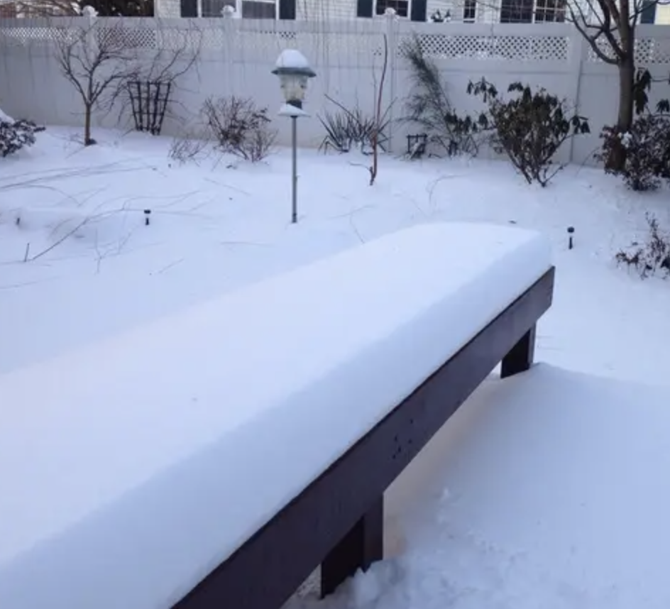 Backyard covered in snow with a thick layer on a bench and a lamp post, winter scene