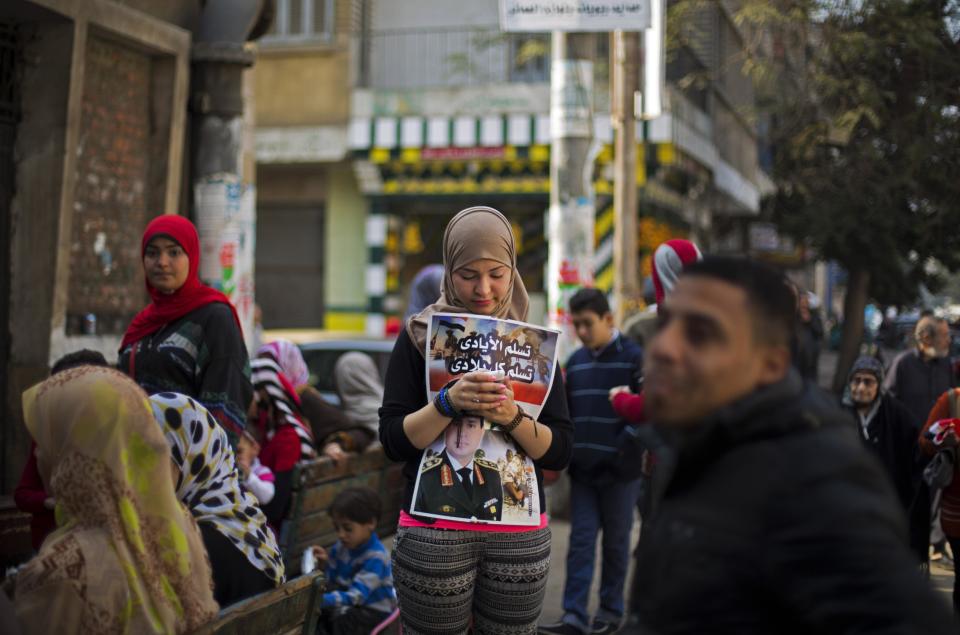 An Egyptian woman holds a poster with a picture of Egypt's Defense Minister, Gen. Abdel-Fattah el-Sissi, as she waits to vote in the country's constitutional referendum in Cairo, Egypt, Tuesday, Jan. 14, 2014. Upbeat and resentful of the Muslim Brotherhood, Egyptians voted Tuesday on a new constitution in a referendum that will pave the way for a likely presidential run by the nation's top general months after he ousted Islamist President Mohammed Morsi. Arabic on the poster reads, "blessed be the hands may my entire homeland be safe." (AP Photo/Khalil Hamra)