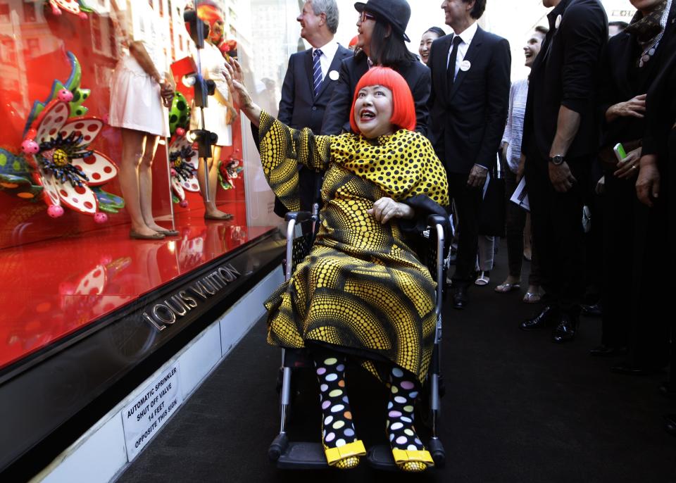 Artista Yayoi Kusama, center poses for photographers with Louis Vuitton CEO Yves Carcelle, upper left, in front of the windows of Vuitton's flagship store for the unveiling of a new collaborative collection by Vuitton creative designer Marc Jacobs and Kusama in New York, Tuesday, July 10, 2012. (AP Photo/Kathy Willens)