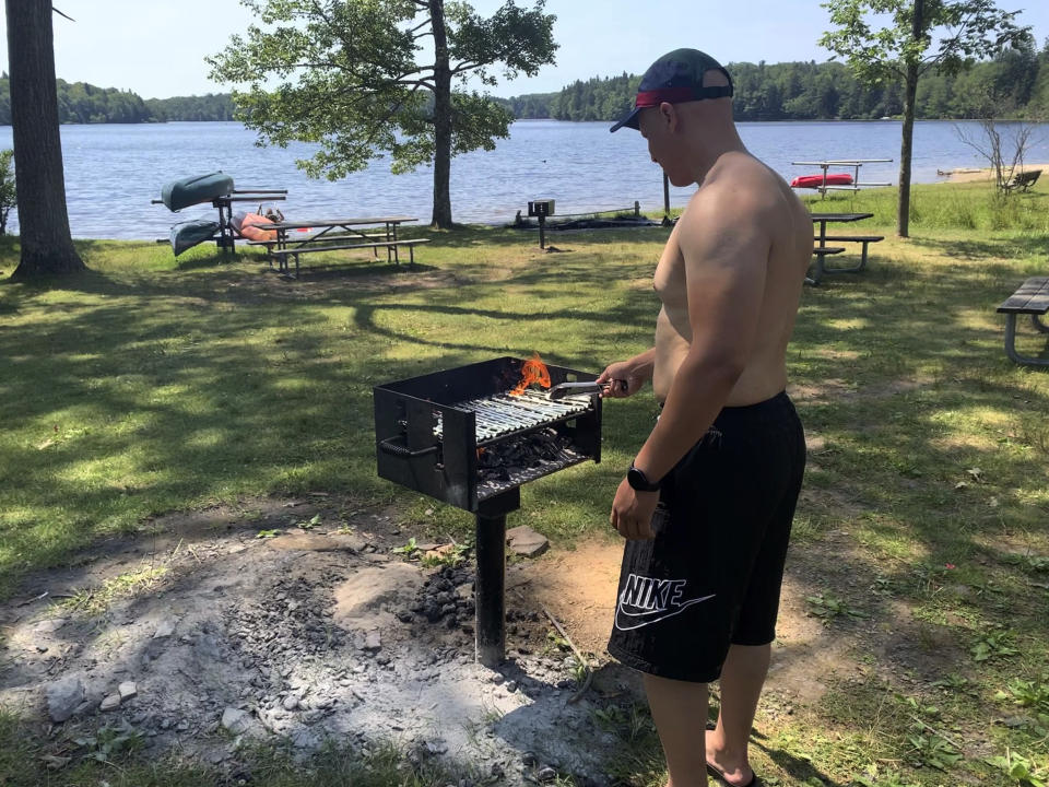 Mhamed Moussa Boudjelthia, of New York City, works a grill Sunday, July 24, 2022 at Promised Land State Park in Pennsylvania's Pocono Mountains in Greentown, Pa. He and friends came to escape the heat in the city. Residents around the Northeast braced for potentially record-breaking temperatures Sunday as a nearly weeklong hot spell continued. (AP Photo/Jeff McMillan)