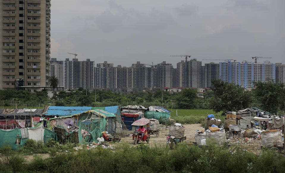 In this Thursday, Sept. 5, 2019, photo, an Indian man drives a battery operated rickshaw through a slum as unfinished residential housing projects are seen in the background in Noida on the outskirts of New Delhi, India. India's economy, once one of the fastest growing in the world, is braking in a blow to the labor-intensive manufacturing sector. Growth slipped to 5% in the April-June quarter, the slowest pace in six years, and many economists believe that Prime Minister Narendra Modi's signature economic policies are at least partly to blame. (AP Photo/Altaf Qadri)