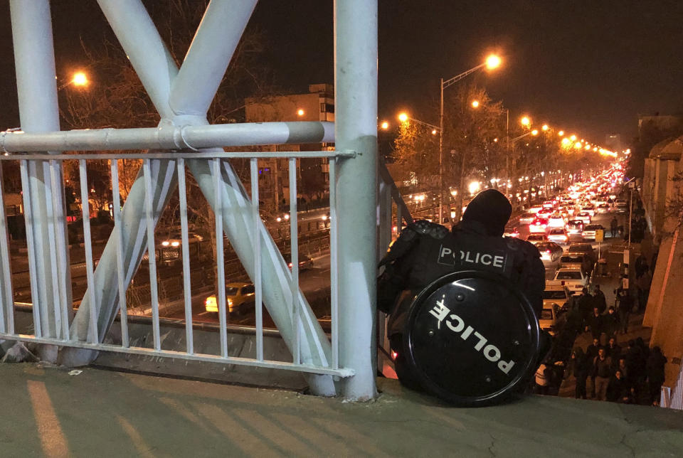 In this photograph taken Sunday, Jan. 12, 2020, a riot police officer watches protesters demonstrating to remember victims of a Ukrainian airplane shot down by an Iranian missile in Tehran, Iran. On Monday, Jan. 13, 2020, online videos purported to show that Iranian security forces fired both live ammunition and tear gas to disperse demonstrators protesting against the Islamic Republic's initial denial that it shot down a Ukrainian jetliner. (AP Photo)