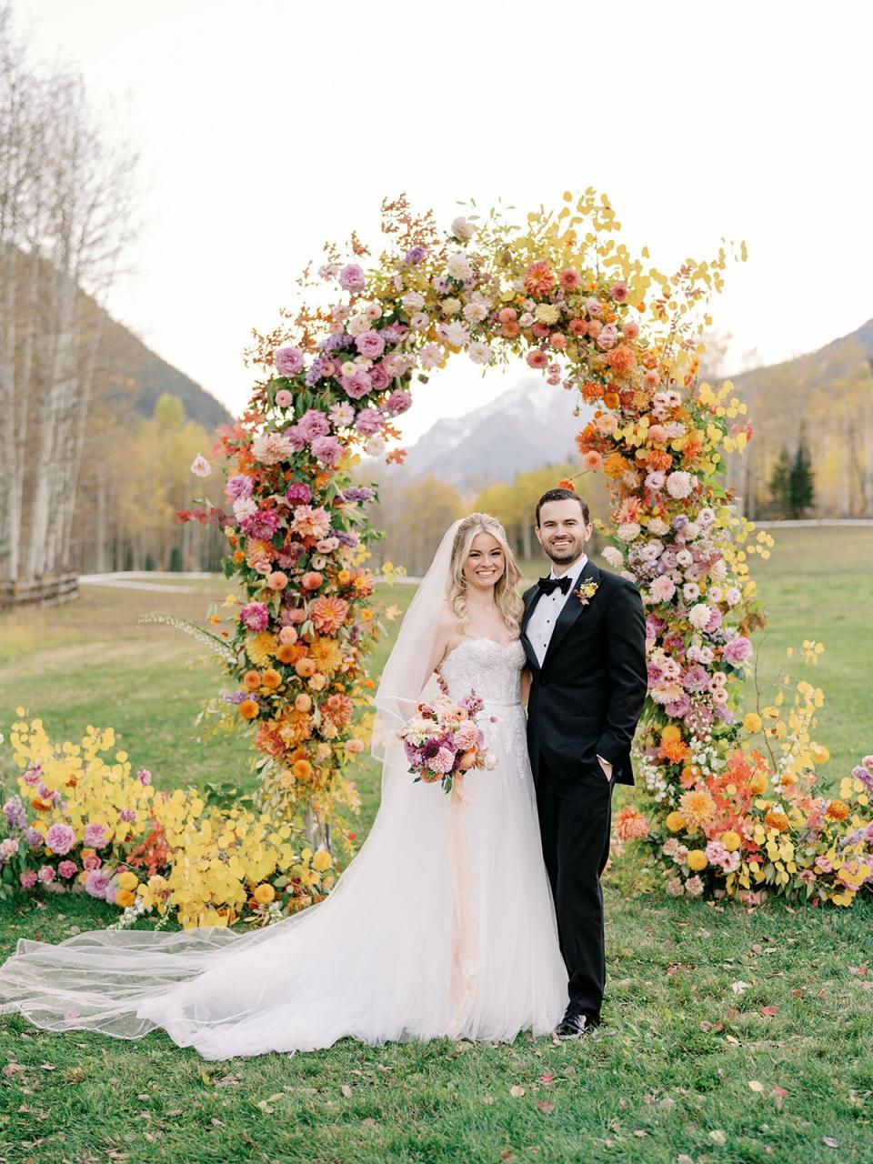 bride and groom smiling under ceremony floral archway