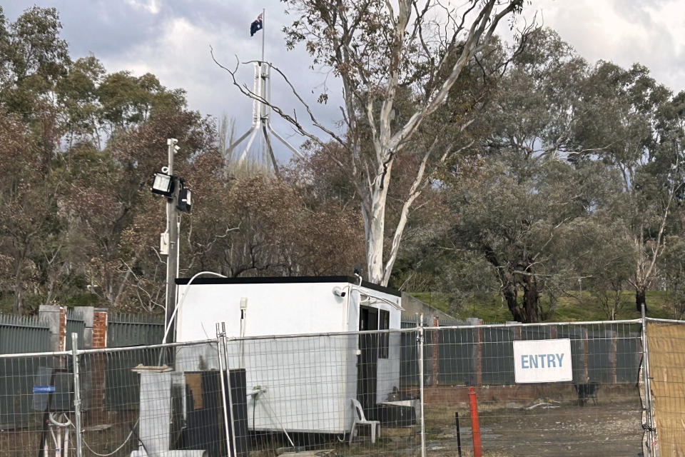 A flag on Australia's Parliament House flys behind where a fence surrounds a building on the grounds of a proposed new Russian embassy in Canberra, Friday, June 23, 2023. A suspected lone Russian diplomat is apparently squatting on the site of the proposed embassy that the Australian government has vetoed. Australian Prime Minister Anthony Albanese dismissed the Russian act of defiance saying a "bloke standing in the cold on a bit of grass in Canberra is not a threat to our national security." (AP Photo/Rod McGuirk)