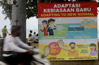 A man rides his motorcycle pass a banner of adapting to coronavirus protection measures at Kuta beach, Bali, Indonesia, Thursday, July 9, 2020. Indonesia's resort island of Bali reopened after a three-month virus lockdown Thursday, allowing local people and stranded foreign tourists to resume public activities before foreign arrivals resume in September. (AP Photo/Firdia Lisnawati)