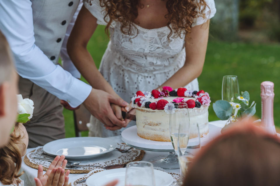 Bride and groom cutting a wedding cake together with guests watching