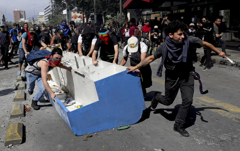 Protesters drag furniture they took from a shop to add to a roadblock amid ongoing demonstrations triggered by an increase in subway fares in Santiago, Chile, Monday, Oct. 21, 2019. Protesters defied an emergency decree and confronted police in Chile’s capital on Monday, continuing disturbances that have left at least 11 dead and led the president to say the country is “at war.” (AP Photo/Miguel Arenas)